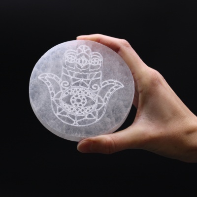 Objeto redondo de pedra branca com símbolo de mão e olho, segurado por uma mão