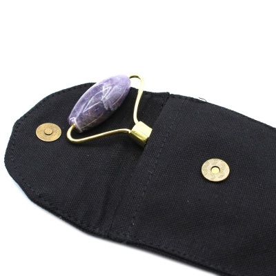 Rolo de massagem facial com pedra roxa e bolsa preta de tecido