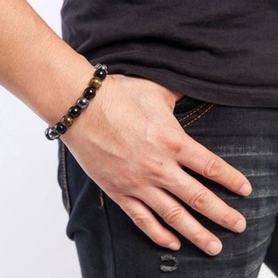 Pulseira masculina de contas pretas e castanhas no pulso esquerdo de uma pessoa com roupa preta