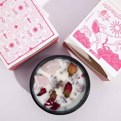 Vela aromática com cristais e pétalas, caixas decorativas brancas e rosa.