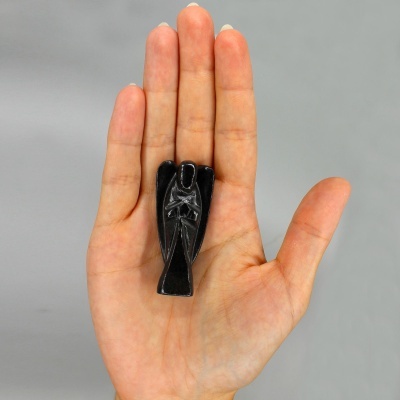Miniatura preta de anjo nas mãos sobre fundo cinzento