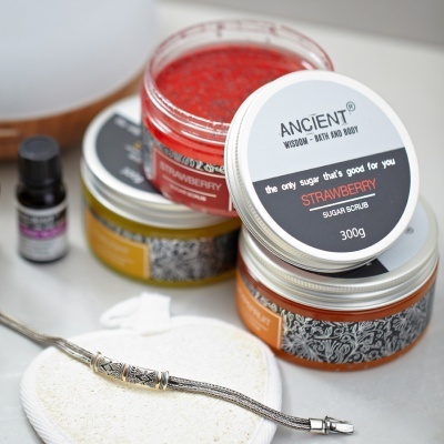 Frascos de esfoliante de açúcar morango da marca ANCIENT com tampas prateadas e um pequeno frasco escuro em superfície branca