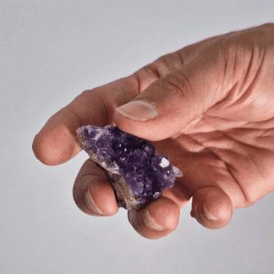 Mão segurando pedra mineral roxa cristalina