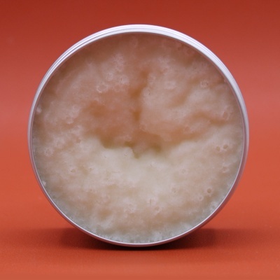 Frasco aberto com creme bege claro em fundo laranja