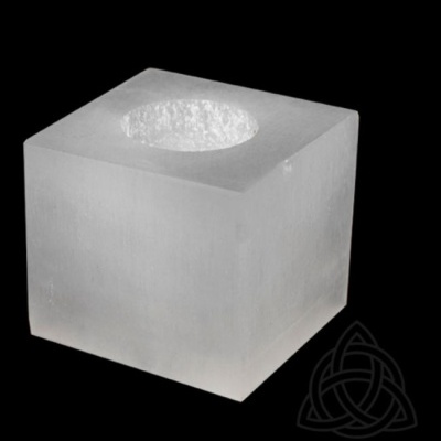 Vela cúbica branca translúcida com buraco circular no topo sobre fundo preto com símbolo triquetra