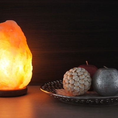 Lâmpada de sal âmbar iluminada e três frutas decorativas num prato prateado