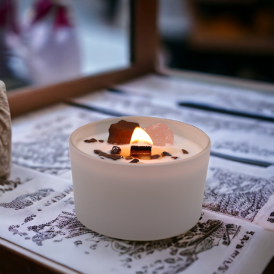 Vela branca acesa num recipiente de cerâmica com pedras e grãos de café sobre superfície decorada.