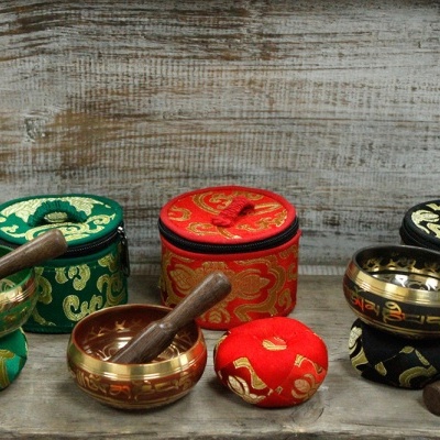 Conjuntos de tigelas tibetanas douradas com almofadas e martelos em verde, vermelho e preto sobre madeira.
