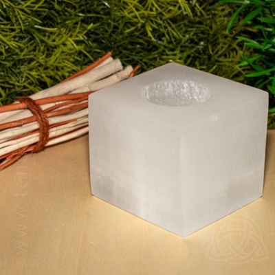 Castiçal cúbico de selenite branca com feixe de paus e folhagem verde ao fundo