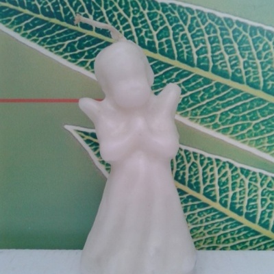 Vela branca em forma de anjo com fundo de folhas verdes