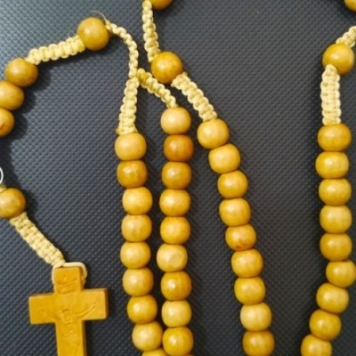Rosário de contas de madeira amarelas com cruz de madeira em fundo preto.
