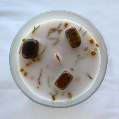 Vela branca com pedras decorativas e ramos secos num recipiente de vidro