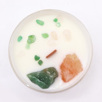 Vela branca com pedras coloridas e pauzinho em recipiente de vidro