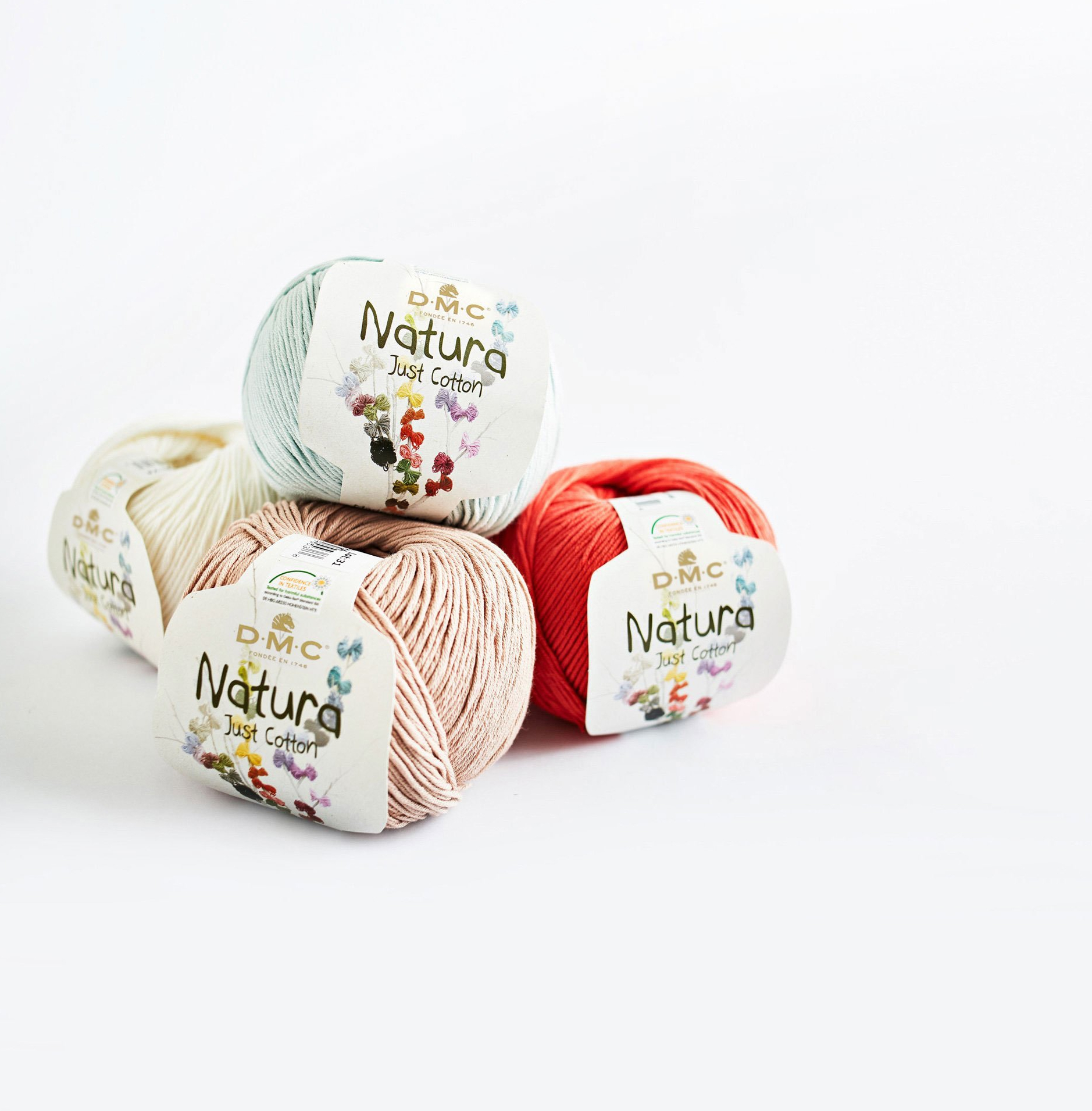 Quatro novelos de fio de algodão DMC Natura em cores variadas sobre fundo branco.