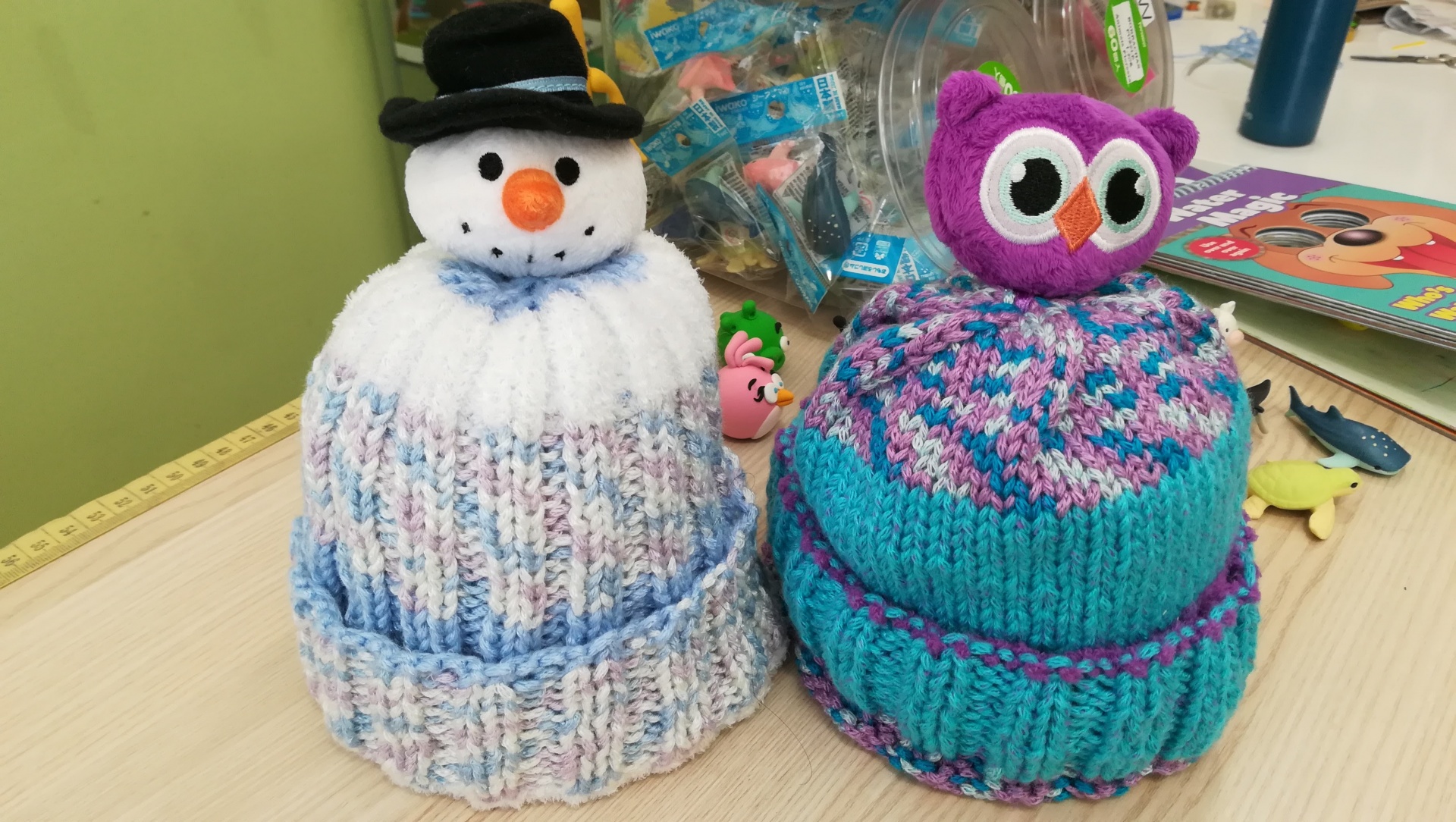 Dois gorros de malha com boneco de neve e coruja em cima numa mesa de madeira