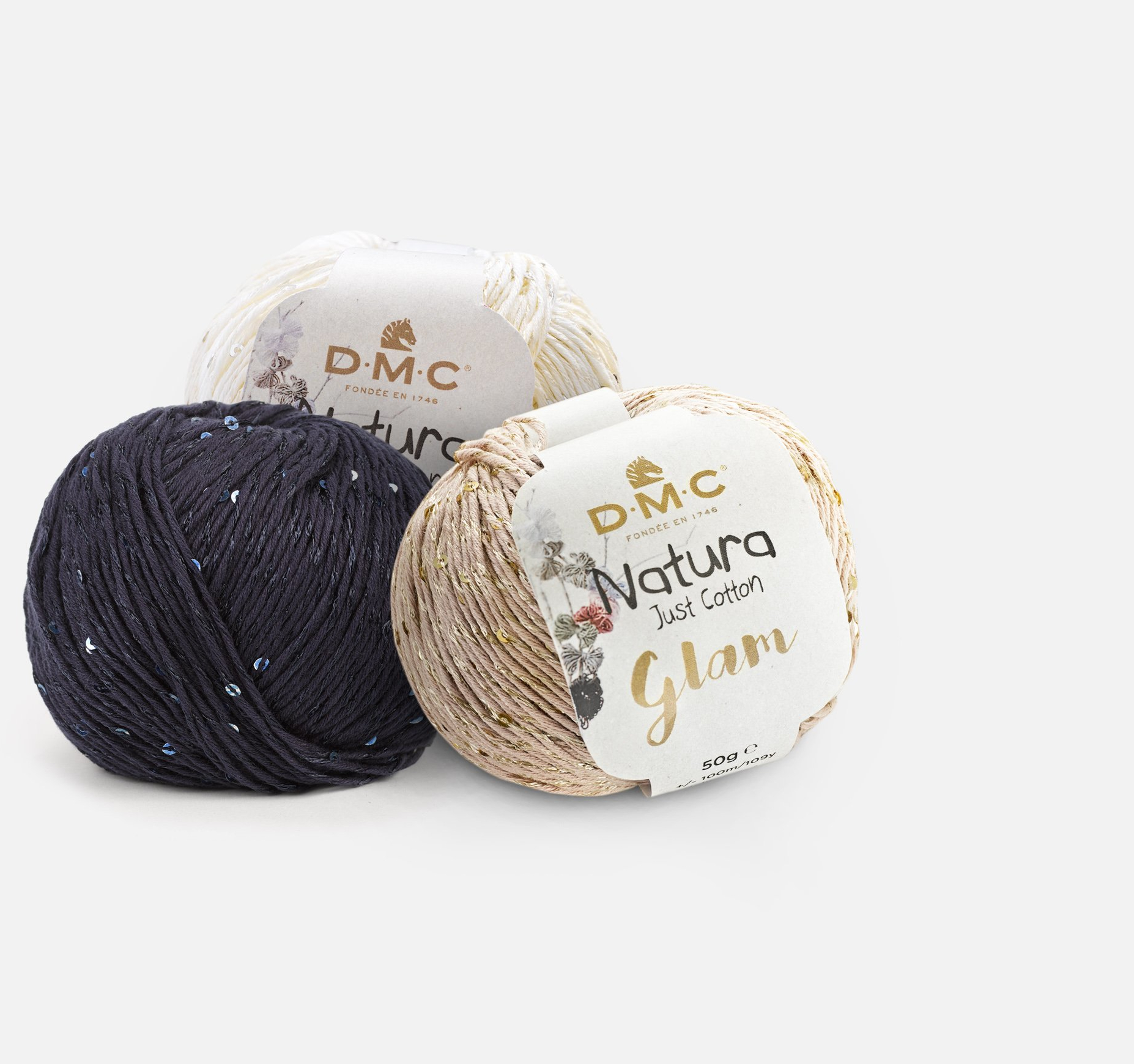 Três novelos de fio DMC Natura Just Cotton Glam em cores variadas com etiqueta e fundo branco.