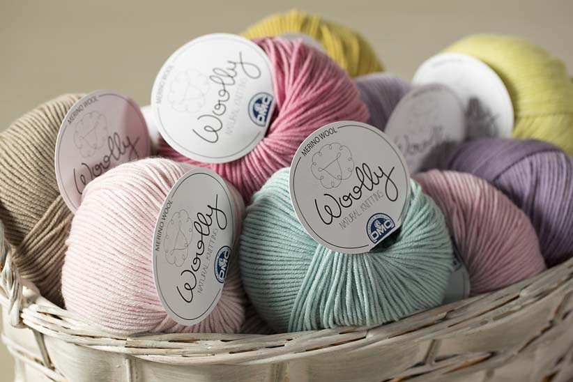 Vários novelos coloridos de lã com rótulo Woolly em cesto de vime