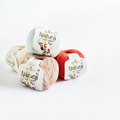 Quatro novelos de fio de algodão DMC Natura em cores variadas sobre fundo branco.
