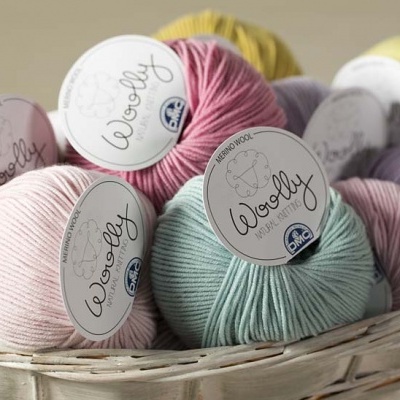 Vários novelos coloridos de lã com rótulo Woolly em cesto de vime