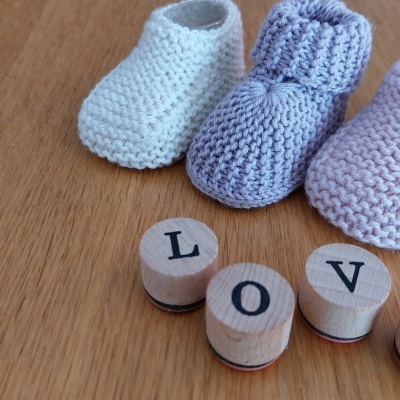 Botinhas de bebé em croché branco, azul claro e rosa com blocos de madeira a formar LOVE sobre superfície de madeira