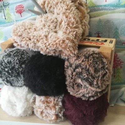 Novelos de lã felpuda multicolor em superfície clara com tecido estampado de árvores e casas ao fundo