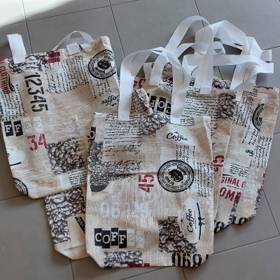 Três sacos de tecido com padrão de texto e números em preto e vermelho com alças brancas