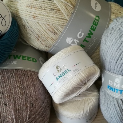 Novelos de lã de várias cores com etiquetas visíveis, sobre uma mesa