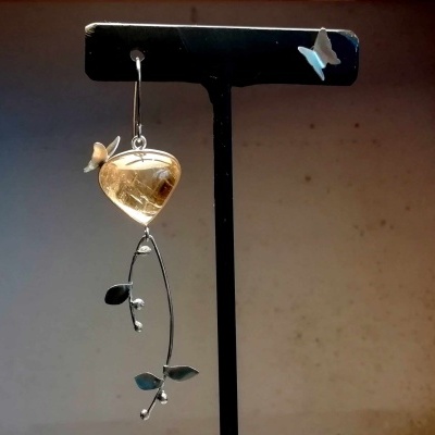 Brinco pendente com pedra amarela e detalhes metálicos em suporte preto