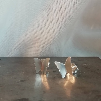 Brincos de borboleta em metal prateado sobre pedra escura
