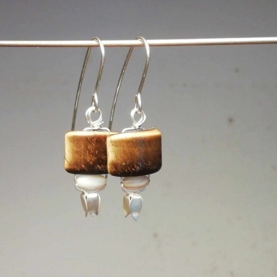 Brincos pendentes com madeira castanha e pedras brancas em fundo neutro
