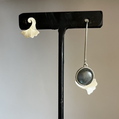 Par de brincos pendurados em suporte preto, metal prateado com design assimétrico