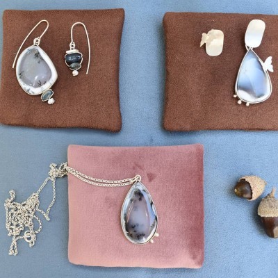 Jóias com pedras cinza e brancas em almofadas de tecido castanho e rosa, com bolotas ao lado.