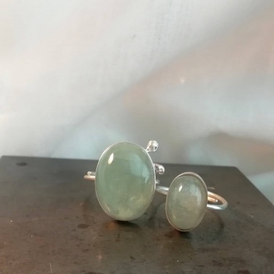 Anel com duas pedras verdes ovais e estrutura metálica prateada