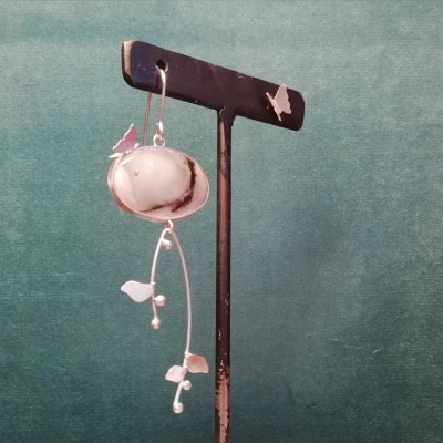 Brinco pendente com pedra branca e detalhes metálicos em suporte preto