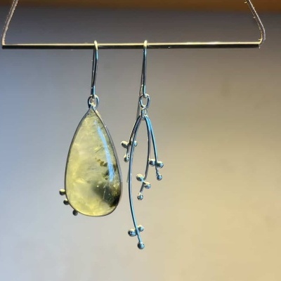 Brincos assimétricos, um com gota de pedra amarela translúcida e outro com design metálico prateado