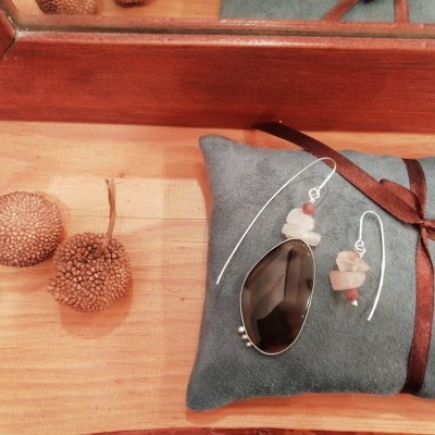 Conjunto de joalharia com pendente e brincos em metal prateado com pedra preta em almofada azul.