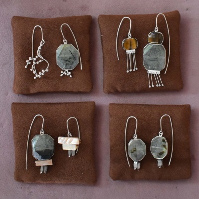Quatro pares de brincos com pedras e metal prateado em almofadas castanhas