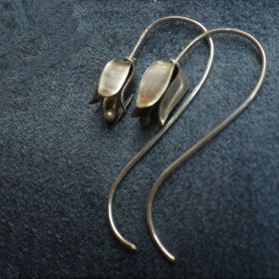 Par de brincos metálicos prateados em forma de flor sobre tecido azul escuro