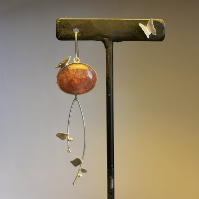 Brinco pendente com pedra oval laranja, estrutura metálica com folhas douradas e borboletas em suporte preto