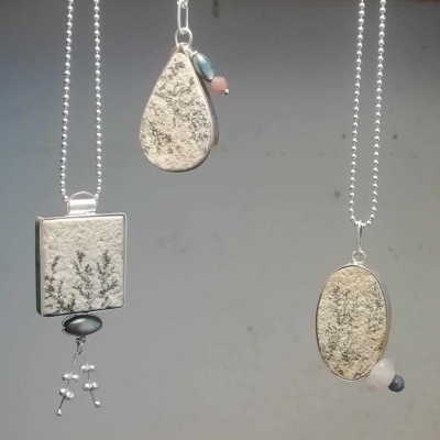 Três colares com pedras naturais em formas oval, lágrima e quadrado, cada um com penduricalhos coloridos e correntes metálicas.