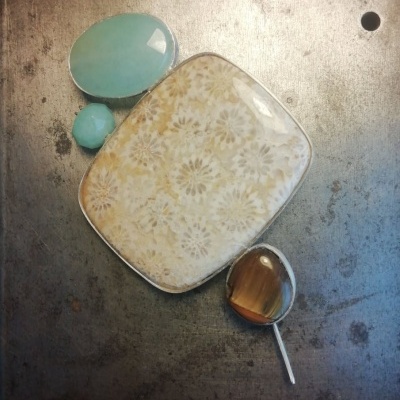 Broche com pedras coloridas em azul, bege e castanho sobre superfície metálica cinzenta