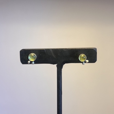 Brincos pequenos com pedra verde e pendentes metálicos em suporte preto