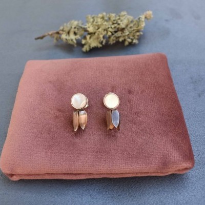 Brincos com base branca e peças penduradas em ouro rosa e azul sobre suporte de veludo cor de rosa