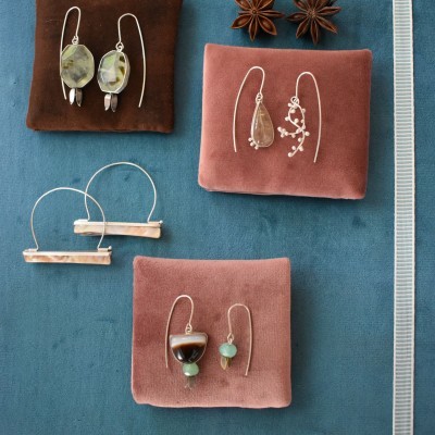 Quatro pares de brincos em almofadas de tecido, com pedras e metal prateado, sobre superfície azul