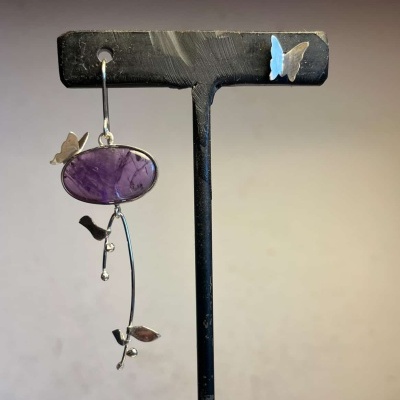 Brinco com pedra roxa e elementos de borboletas e folhas em suporte preto