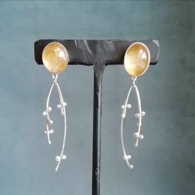 brincos pendentes com base oval amarela e detalhes prateados num suporte preto