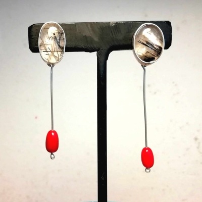 Brincos pendentes com pedra oval translúcida e detalhe vermelho em expositor preto