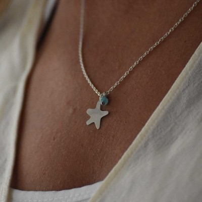 Colar com pendente estrela prateada e pedra azul sobre pele e camisa branca