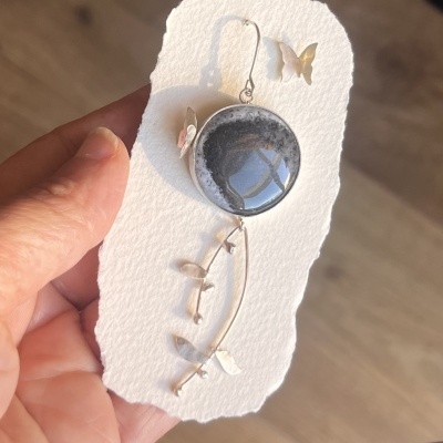 Brinco pendente com pedra preta e decoração prateada em cartão branco