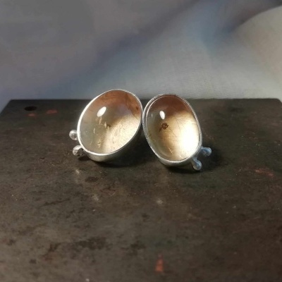 Dois pequenos espelhos côncavos de metal prateado sobre superfície escura